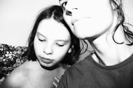 A black and white close-up photograph depicting two individuals in an intimate and emotional pose. One person has their eyes closed and appears thoughtful, while the other person’s face is partially visible, with their gaze directed out of frame. The lighting is high-contrast, lending a dramatic effect.