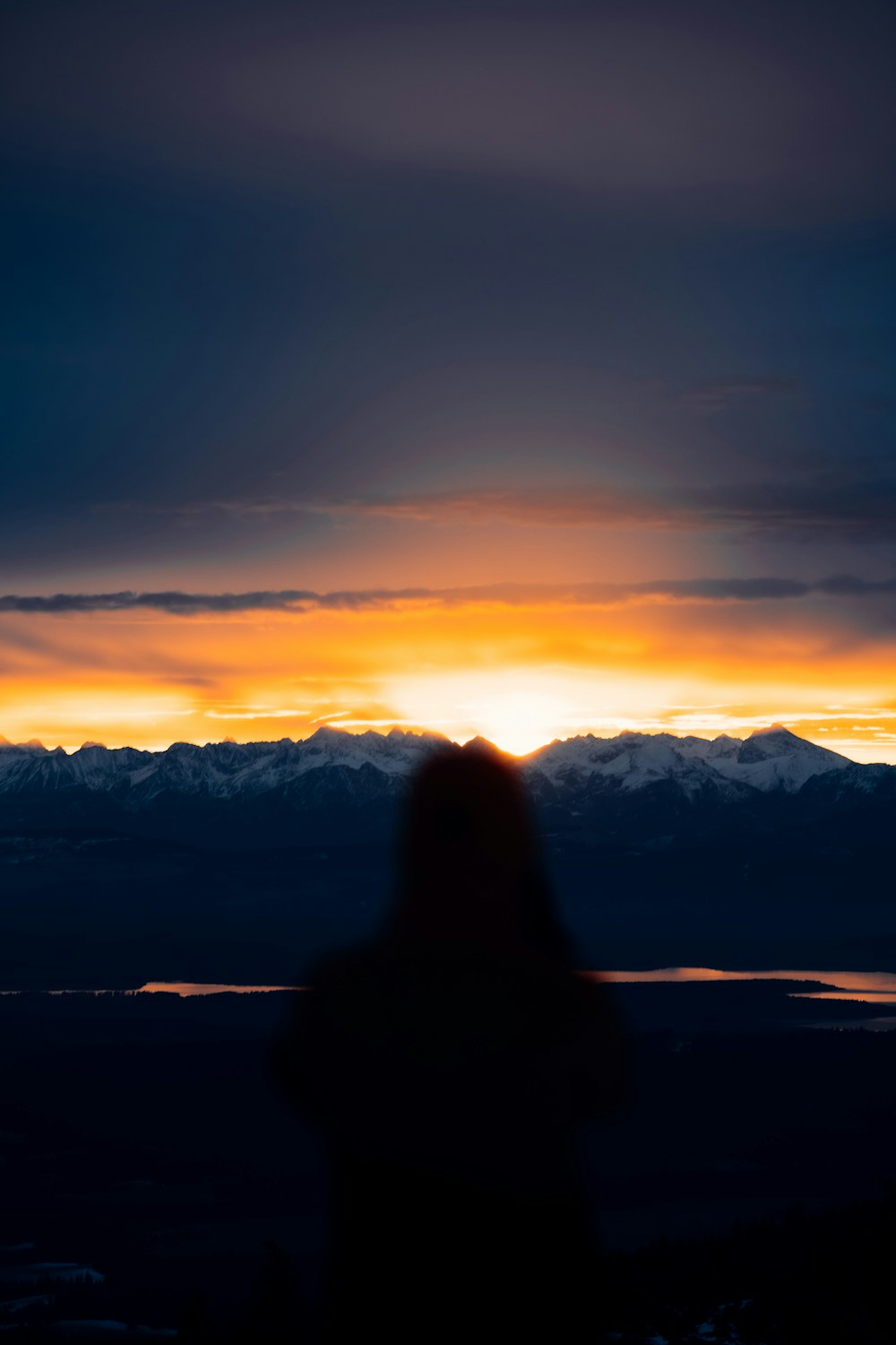 a person standing in front of a sunset with mountains in the background
