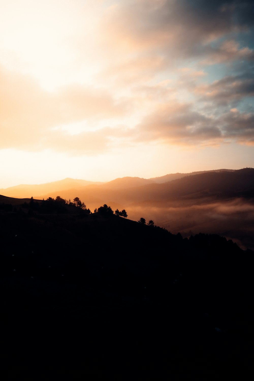 the sun is setting over the hills and trees