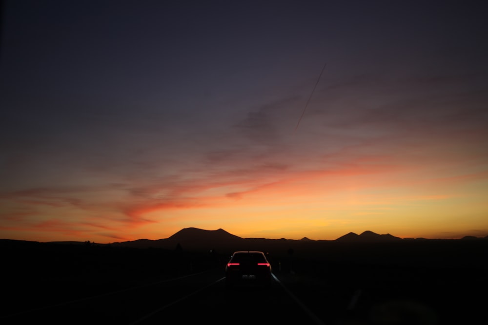 a car driving down a road with a sunset in the background