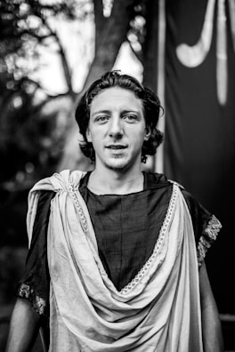 A professional portrait of a male influencer dressed in period costume against a muted earth tone backdrop.