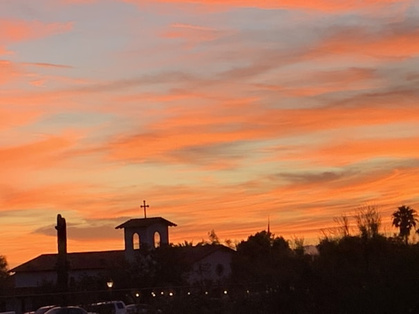 A vibrant orange sunset behind a silhouette of a cross on a hill.