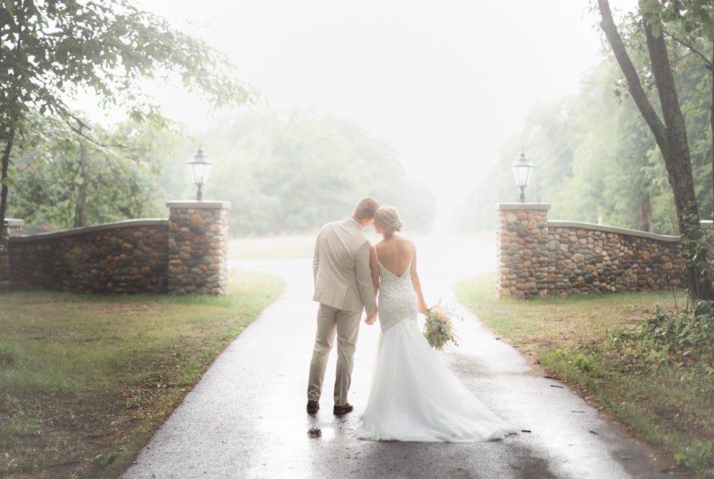 a bride and groom walking down a path in the rain