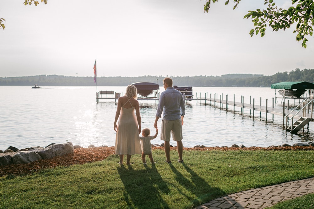 a man and a woman are standing on the grass by the water