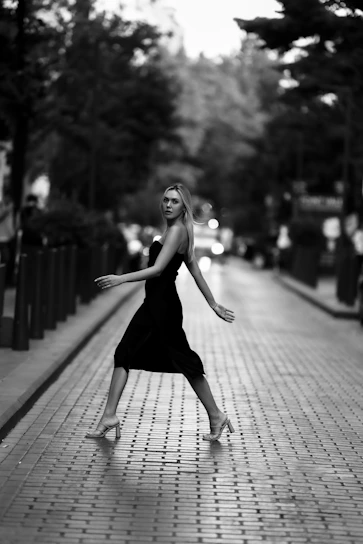 A stylish woman wearing a trendy black dress standing confidently in an urban setting.