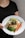 A person holding a plate with a gourmet meal that includes a grilled chicken breast topped with herbs, steamed green beans, roasted carrots, and a lemon wedge, all served over a creamy sauce.