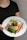 A person holding a plate with a gourmet meal that includes a grilled chicken breast topped with herbs, steamed green beans, roasted carrots, and a lemon wedge, all served over a creamy sauce.