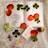 An arrangement on lace fabric featuring pressed clover leaves, rose petals, a floral sketch on paper, a small decorative pouch, a cross pendant box, a colorful beaded cross, crystals, and a small cork bottle with decorative faux flowers.