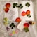 An arrangement on lace fabric featuring pressed clover leaves, rose petals, a floral sketch on paper, a small decorative pouch, a cross pendant box, a colorful beaded cross, crystals, and a small cork bottle with decorative faux flowers.