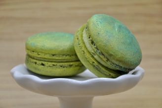 A vibrant emerald green macaron with delicate pistachio crumbs on a white ceramic plate.