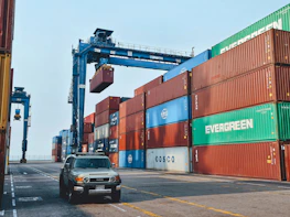 A shipping container being carefully loaded with a luxury vehicle at a busy port.