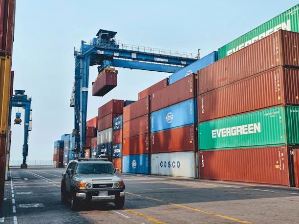 Stacks of shipping containers being carefully loaded by cranes at a busy port.