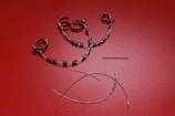 A collection of orthodontic appliance components laid out on a textured red surface. The items include metal braces with brackets and wire loops, a coil spring, and curved wires.