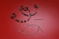 A collection of orthodontic appliance components laid out on a textured red surface. The items include metal braces with brackets and wire loops, a coil spring, and curved wires.