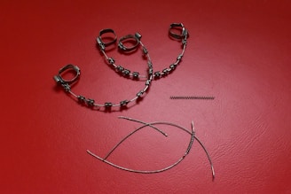 A collection of orthodontic appliance components laid out on a textured red surface. The items include metal braces with brackets and wire loops, a coil spring, and curved wires.