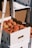 Cardboard boxes filled with ripe peaches stacked on top of each other. The boxes are white with open handles, allowing a glimpse of the fruit inside. Sunlight creates subtle shadows on the boxes, enhancing the texture and colors of the peaches.