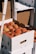 Cardboard boxes filled with ripe peaches stacked on top of each other. The boxes are white with open handles, allowing a glimpse of the fruit inside. Sunlight creates subtle shadows on the boxes, enhancing the texture and colors of the peaches.