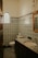 A bathroom with intricate, multicolored patterned tiles covering the walls and floor. The room features a sink with a wooden-framed mirror above it and a round window with a decorative pattern.