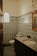 A bathroom with intricate, multicolored patterned tiles covering the walls and floor. The room features a sink with a wooden-framed mirror above it and a round window with a decorative pattern.