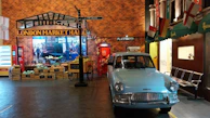 A stylish vintage car parked beside a colorful street market, with vibrant banners fluttering overhead.