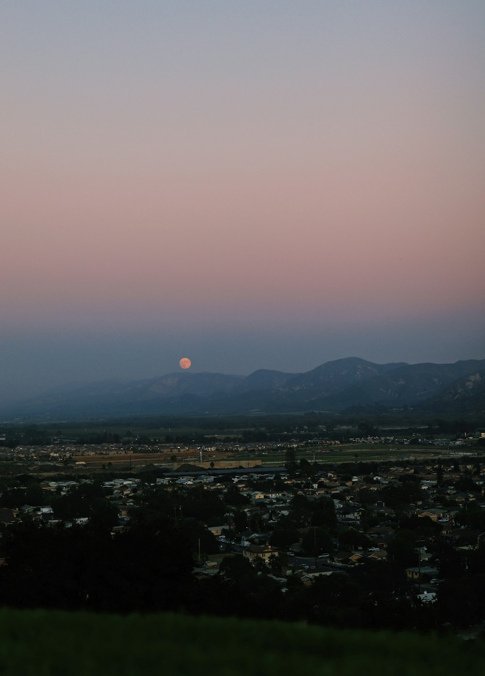 the sun is setting over a city with mountains in the background