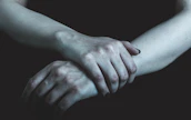 Close-up of hands intertwined, charcoal shadows playing softly on warm skin tones.
