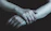 Moody close-up of dimly lit hands entwined in leather straps against a deep blue background.