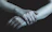 Moody close-up of dimly lit hands entwined in leather straps against a deep blue background.