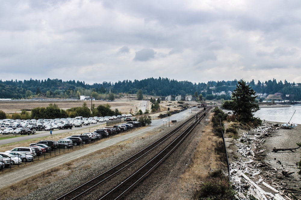 a train track with cars parked on it next to a body of water