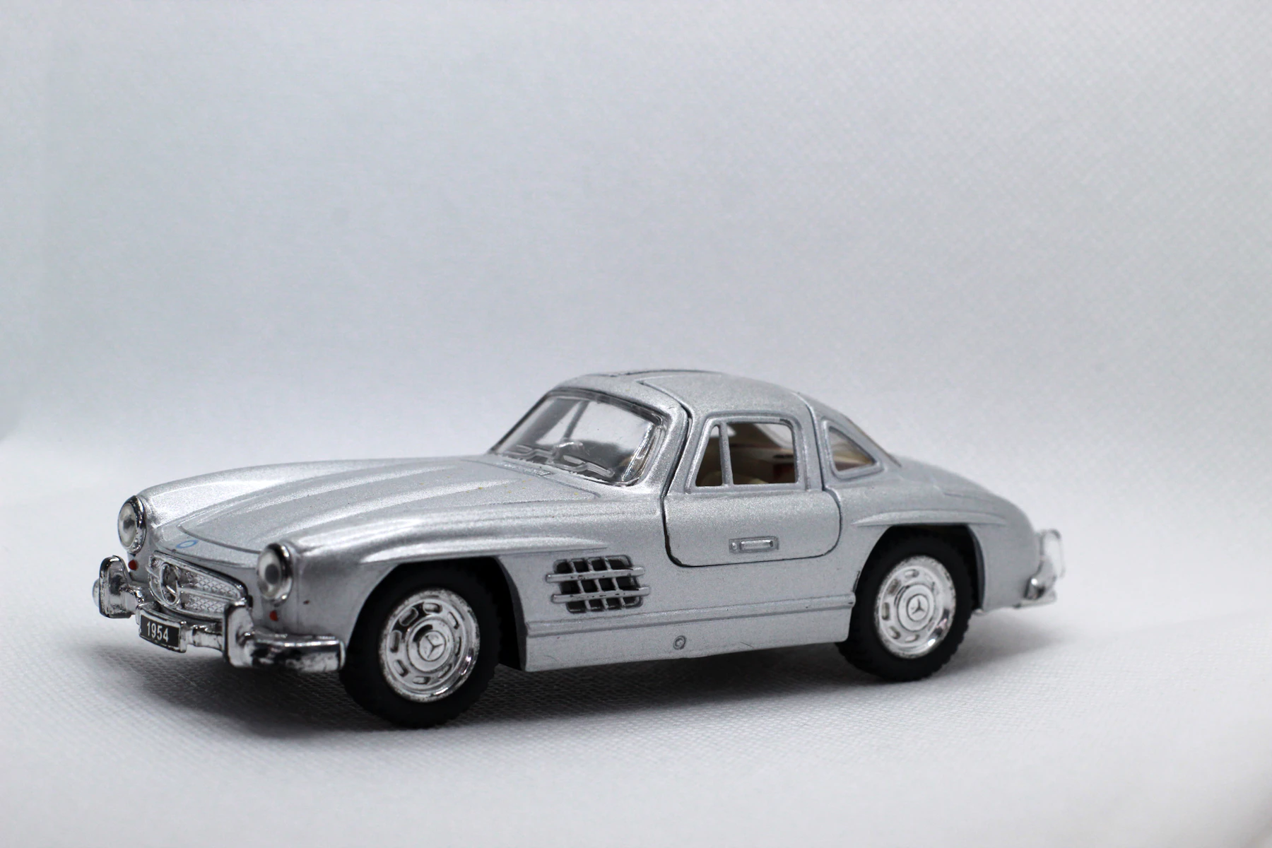 A silver die-cast model of a gullwing coupe, side on, on a white background