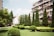 A residential area features apartment buildings adorned with numerous balconies and air conditioning units. In the foreground, a well-maintained garden displays neatly trimmed bushes and tall, conical evergreen trees, all under a clear blue sky.