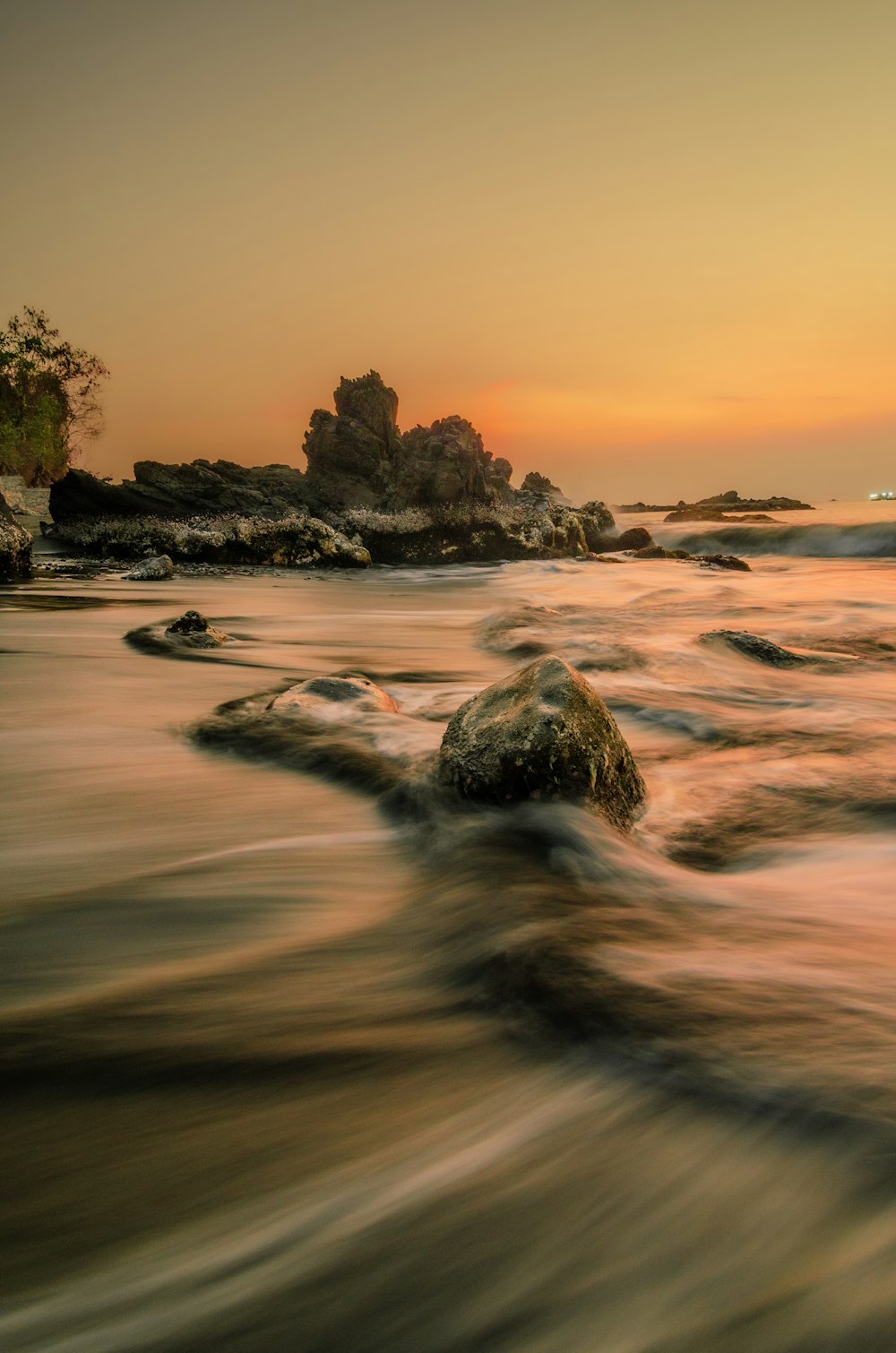 a rock in the water with a sunset in the background