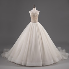 A mannequin displays an elegant white ball gown with a fitted bodice adorned with intricate beadwork and a voluminous layered skirt.
