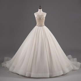 A mannequin displays an elegant white ball gown with a fitted bodice adorned with intricate beadwork and a voluminous layered skirt.