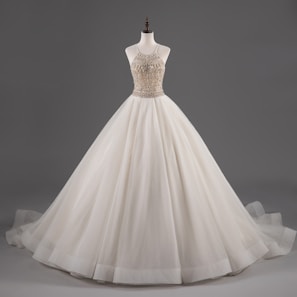 A mannequin displays an elegant white ball gown with a fitted bodice adorned with intricate beadwork and a voluminous layered skirt.