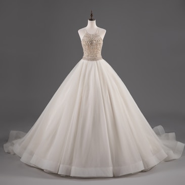 A mannequin displays an elegant white ball gown with a fitted bodice adorned with intricate beadwork and a voluminous layered skirt.