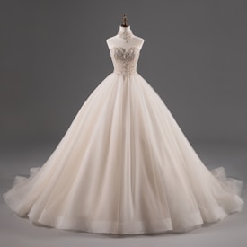 A luxurious, strapless ball gown with intricate lace detailing on the bodice, featuring a voluminous tulle skirt. The dress is displayed on a mannequin against a plain grey background.