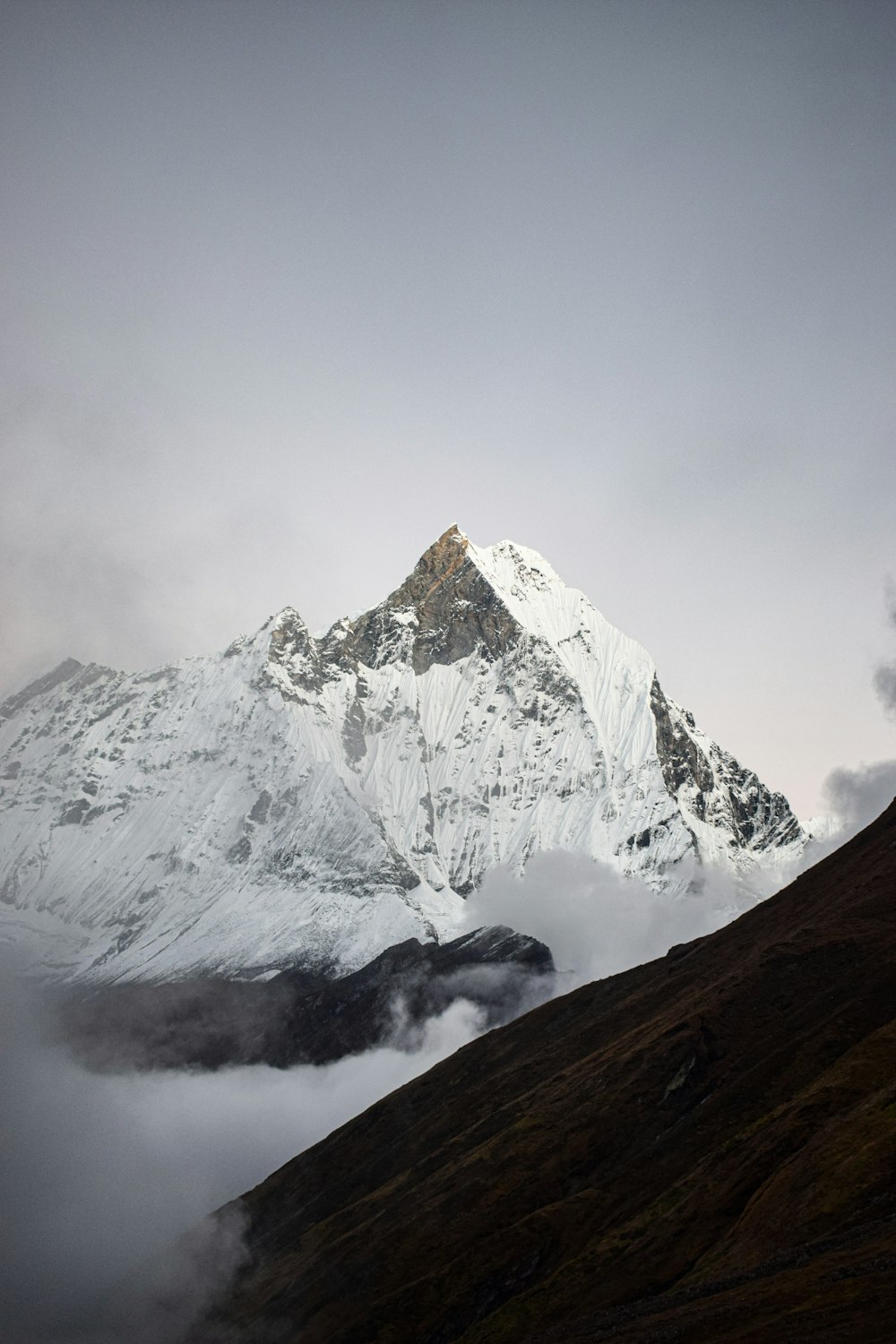 a mountain covered in snow and clouds on a cloudy day