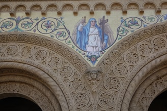 A detailed architectural design featuring intricate carvings and a mosaic depicting a figure in a robe holding a cross and a banner reading 'FAITH'. The mosaic is surrounded by floral patterns in vibrant colors.