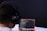 A person with headphones is engaged in coding on a laptop. The screen displays lines of code, possibly written in a programming language like JavaScript or Python. The setting has a minimalistic and focused atmosphere, with a dark background.