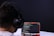 A person with headphones is engaged in coding on a laptop. The screen displays lines of code, possibly written in a programming language like JavaScript or Python. The setting has a minimalistic and focused atmosphere, with a dark background.