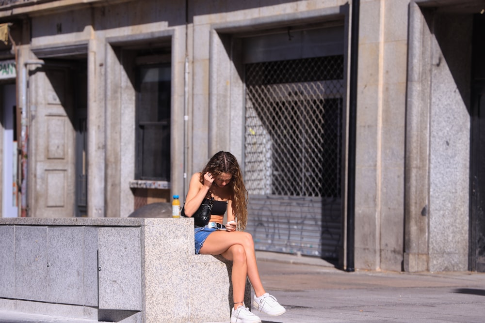 a woman sitting on a ledge looking at her cell phone