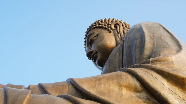 Close-up low-angle view of the bronze Tian Tan Big Buddha's head and shoulder against a clear blue sky.