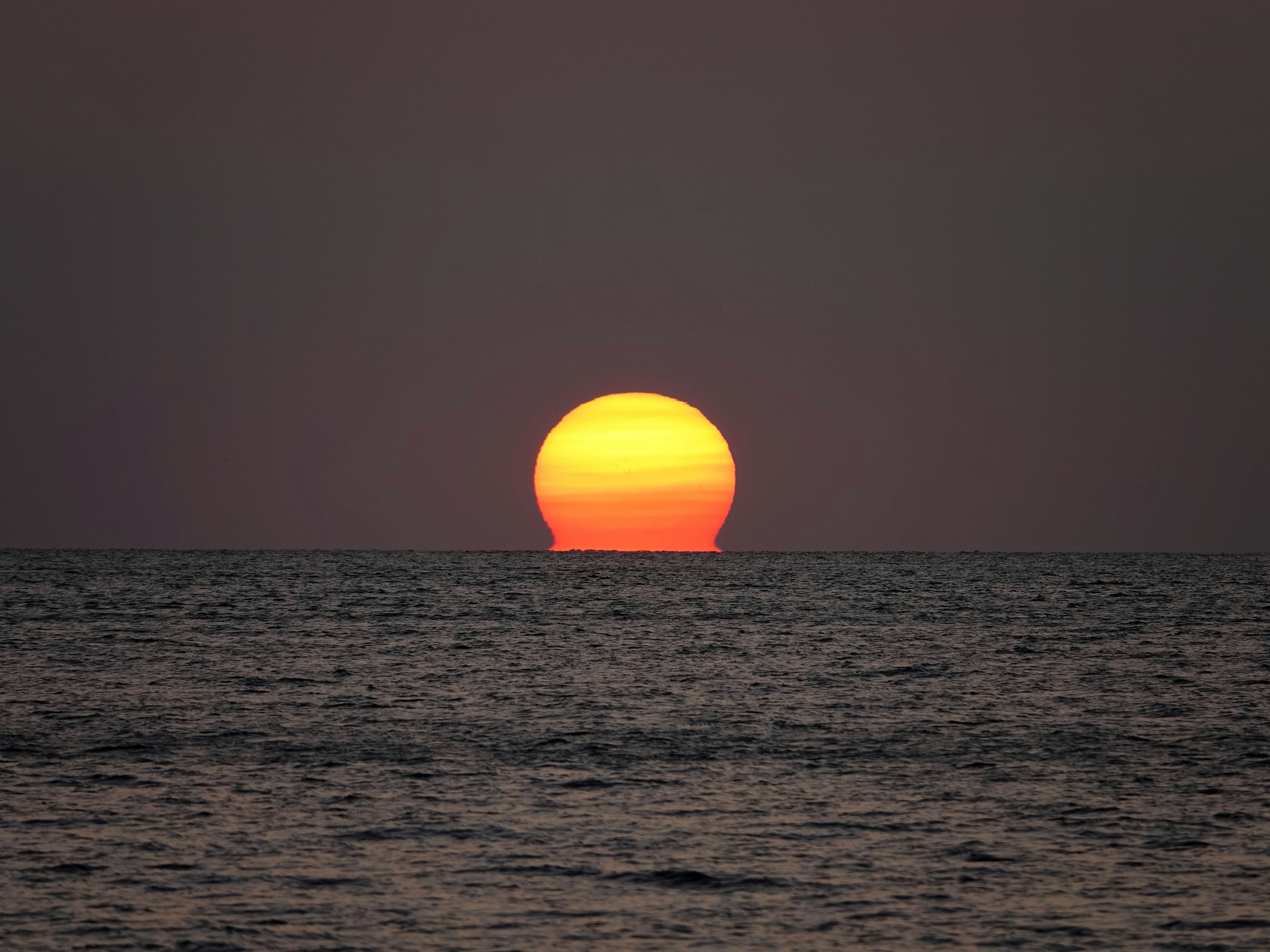 the sun setting over the ocean with a boat in the distance