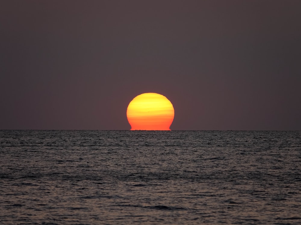 the sun setting over the ocean with a boat in the distance