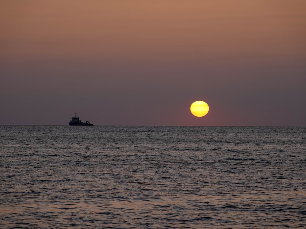 the sun is setting over the ocean with a boat in the distance