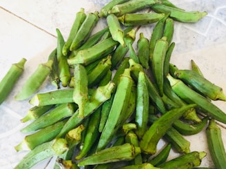 A collection of fresh green okra pods spread out on a light-colored surface, showcasing various sizes and natural textures.