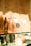 Several brown paper coffee bags are lined up on a glass shelf, each with a label indicating the brand 'Coffee & Water Lab' and specific details about the coffee. The labels feature a graphic of a coffee dripper. The scene is warmly lit, giving a cozy and inviting ambiance.