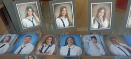 A collection of framed and unframed portrait photographs displayed on a glass surface, primarily featuring young adults in formal attire, likely school or graduation photos. The images show individuals wearing white shirts and dark ties, suggesting a uniform or dress code.