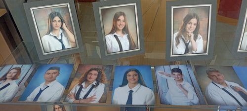 A collection of framed and unframed portrait photographs displayed on a glass surface, primarily featuring young adults in formal attire, likely school or graduation photos. The images show individuals wearing white shirts and dark ties, suggesting a uniform or dress code.
